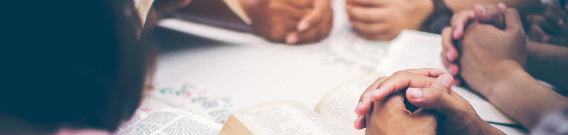 Group of people at a table with open bibles, praying